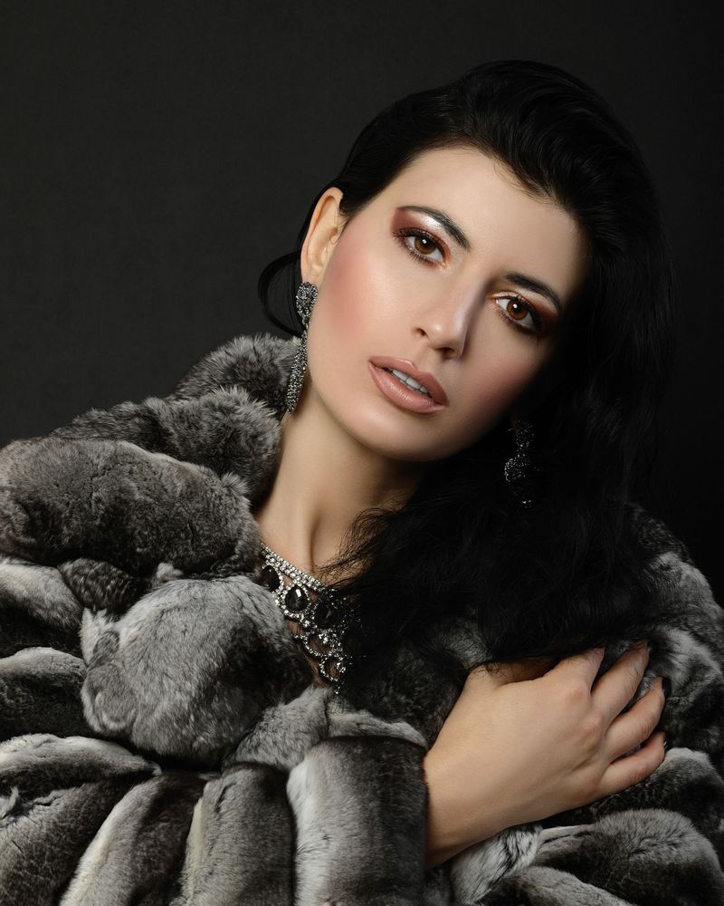 Model wrapped in a plush grey faux fur coat with a statement necklace against a dark studio backdrop
